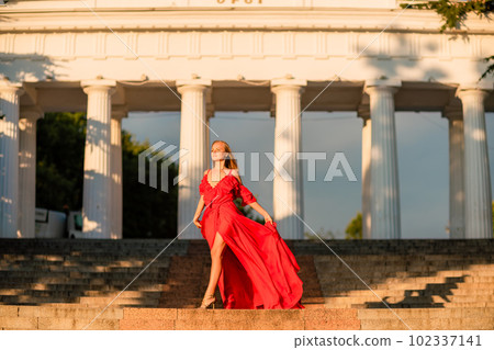A woman in a long red dress against the backdrop of sunrise, bright golden light of the sun's rays. The concept of femininity, harmony. 102337141