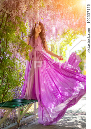 Woman wisteria lilac dress. Thoughtful happy mature woman in purple dress surrounded by chinese wisteria 102337156