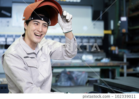 一個穿著工作服、戴著面具的微笑男子用於弧焊等。 102339011