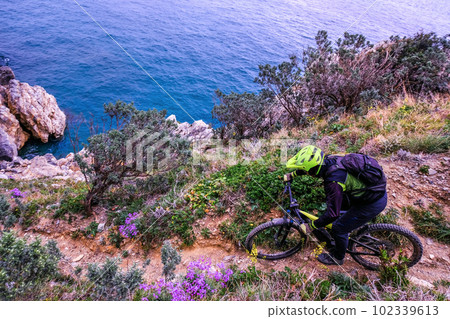 Unrecognisable mountain biker descends on a challenging trail steep towards the sea, Finale Ligure, Italy Unrecognisable mountain biker descends on a challenging trail steep towards the sea, Finale Ligure, Italy 102339613