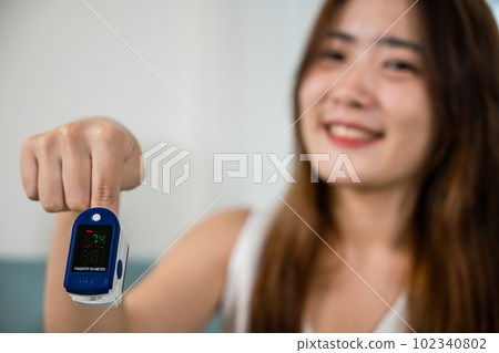 Young woman finger inserted into the pressure oximeter to assess health under sofa in living room at home, Self healthcare with corona virus pandemic, medical health care concept 102340802