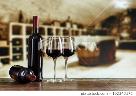 A bottle of wine and glasses with wine on a barrel in a wine cellar. 102343175