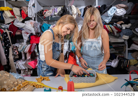 A designer and a student look for buttons for a selected fabric in a tailor's shop. 102344529