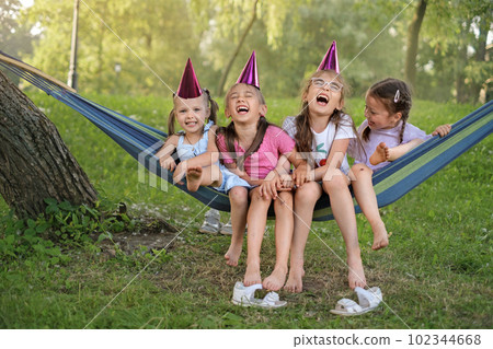 A group of children are laughing merrily sitting on a hammock in the park celebrating a friend's birthday. Happy funny kids relaxing in the backyard A group of children are laughing merrily sitting on a hammock in the park celebrating a friend's birthday. Happy funny kids relaxing in the backyard 102344668