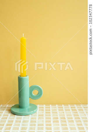 Candle on check tile table. yellow wall background. home interior 102347778