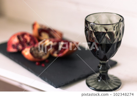 Pomegranate with glass of wine on table. Cut pomegranate with seeds and red wine. Fruits and wine. Summer still life. Alcohol drinks and juicy ripe pomegranate. Vintage glass of wine and fruits. Pomegranate with glass of wine on table. Cut pomegranate with seeds and red wine. Fruits and wine. Summer still life. Alcohol drinks and juicy ripe pomegranate. Vintage glass of wine and fruits. 102348274