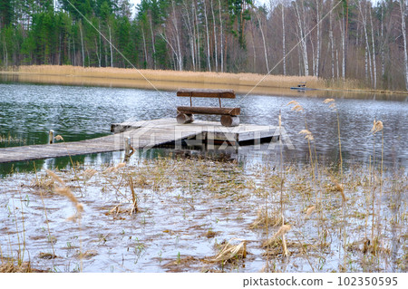 Wooden bench on the tourist site by the lake. Wooden bench on a wooden footbridge in the lake. Fishing place. Wooden bench on the tourist site by the lake. Wooden bench on a wooden footbridge in the lake. Fishing place. 102350595