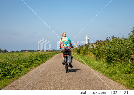 Older woman with camera bag biking on a electric bike in Sassenheim in the Netherlands. 102351211