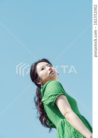 A woman with an ennui expression wearing a green dress against the blue sky 102352002