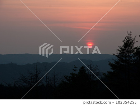 At dusk in summer, the combination of silhouetted mountains and bright red sun is beautiful. 102354253