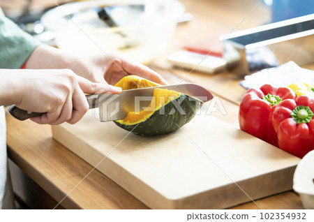 A woman's hand cutting a wrenched pumpkin with a kitchen knife 102354932