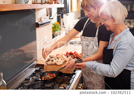 Grandmother, woman and cooking together in kitchen or teach recipe, prepare dinner or lunch with family. Senior mother, daughter and happy in apron or home, food and cook with healthy vegetables 102362511