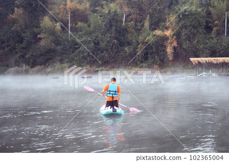man on Paddleboard or sup board in middle of lake and enjoying sunrise and fog in the morning man on Paddleboard or sup board in middle of lake and enjoying sunrise and fog in the morning 102365004