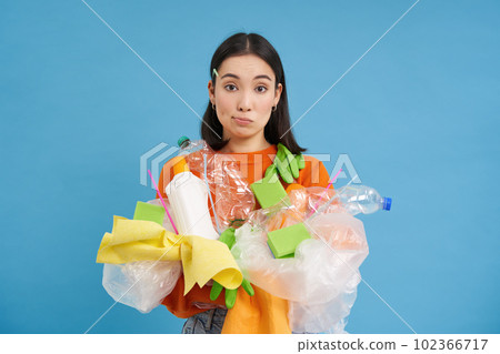 Young confused asian girl with different types of plastic, learns how to recycle, saving enviroment, sorting garbage, blue background 102366717