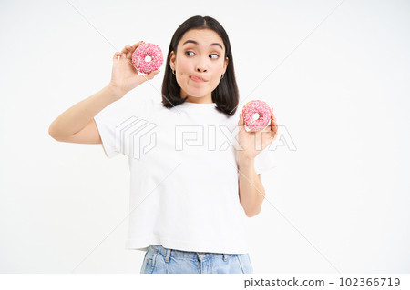 Cute young woman with two tasty doughnuts, tempted to try glazed donnuts, white background 102366719