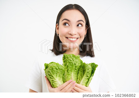Vegetarian nutrition. Smiling happy young woman looks at her self grown cabbage, eating lettuce, white background 102366802