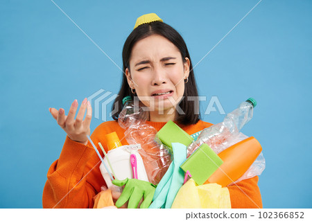 Crying korean woman complaining, holding garbage, plastic bottles, litter, sorting garbage, stressed by recycling, blue background Crying korean woman complaining, holding garbage, plastic bottles, litter, sorting garbage, stressed by recycling, blue background 102366852