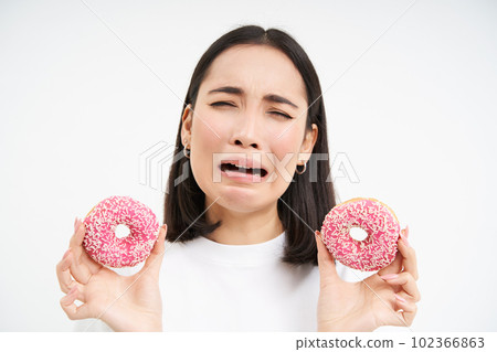 Crying asian woman showing tasty douhnuts and sobbing, being on healthy diet, cant eat junk food, white background 102366863