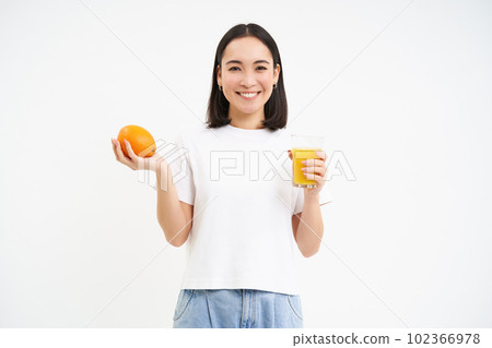 Beautiful and healthy young woman, starts her day with fresh juice, holding orange fruit and smiling, white background Beautiful and healthy young woman, starts her day with fresh juice, holding orange fruit and smiling, white background 102366978