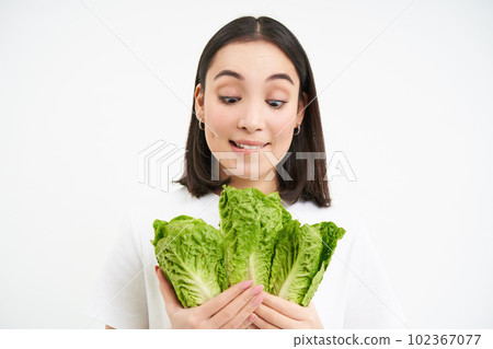 Nutrition and healthy food. Young korean woman looks at tasty fresh cabbage, loves vegetables, white studio background Nutrition and healthy food. Young korean woman looks at tasty fresh cabbage, loves vegetables, white studio background 102367077