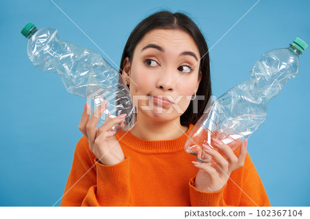 Girl with two plastic bottles, thinking and looking aside, sorting trash, saving planet by recycling, blue background Girl with two plastic bottles, thinking and looking aside, sorting trash, saving planet by recycling, blue background 102367104