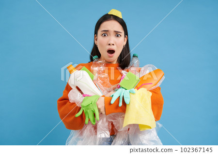 Sad asian woman holding garbage, empty plastic bottles and waste, tired of recycling, sorting rubbish, isolated on blue background Sad asian woman holding garbage, empty plastic bottles and waste, tired of recycling, sorting rubbish, isolated on blue background 102367145