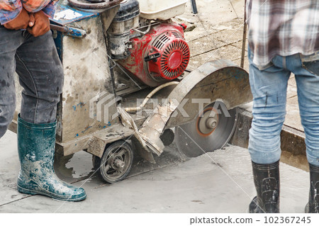 Worker using diamond saw blade machine cutting concrete road at construction site 102367245