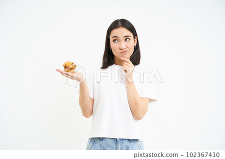 Woman with pensive face, holding cupcake and thinking, white background Woman with pensive face, holding cupcake and thinking, white background 102367410