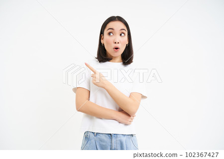 Surprised korean girl, points left and looks with amazed face expression, stands in tshirt isolated on white background Surprised korean girl, points left and looks with amazed face expression, stands in tshirt isolated on white background 102367427