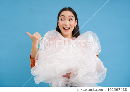 Smiling korean girl shows way to recycling center, sorting waste, holding plastic garbage and pointing left, blue background Smiling korean girl shows way to recycling center, sorting waste, holding plastic garbage and pointing left, blue background 102367488