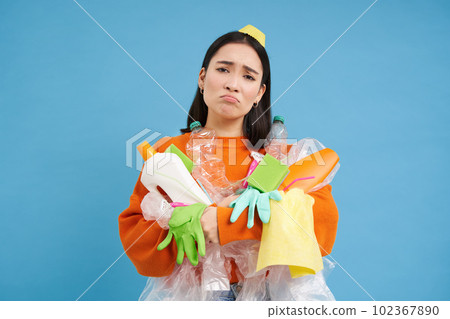 Sad asian woman holding garbage, empty plastic bottles and waste, tired of recycling, sorting rubbish, isolated on blue background 102367890
