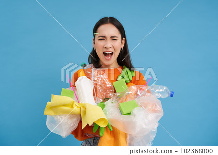 Shocked eco activist, collects loads of plastic to recycle, looking upset at bottles and unsorted garbage, blue background 102368000