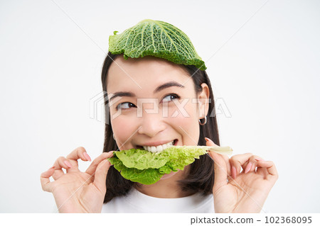 Happy, cute asian woman eating green lettuce, vegetarian likes oranic vegetables, white studio background Happy, cute asian woman eating green lettuce, vegetarian likes oranic vegetables, white studio background 102368095