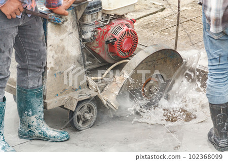 Worker using diamond saw blade machine cutting concrete road at construction site 102368099