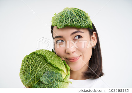 Close up portrait of beautiful and healthy vegan woman, holding lettuce, has cabbage lead on head, white background Close up portrait of beautiful and healthy vegan woman, holding lettuce, has cabbage lead on head, white background 102368385