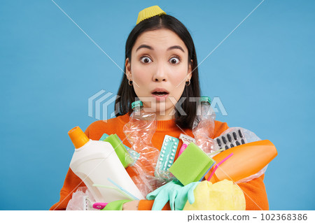 Portrait of girl with shocked face, holds empty plastic bottles, household garbage, stares startled at camera, recycles, blue background Portrait of girl with shocked face, holds empty plastic bottles, household garbage, stares startled at camera, recycles, blue background 102368386