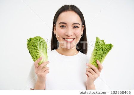 Healthy diet and organic food. Smiling asian woman showing cabbage, eating lettuce, cleansing her body, on detox, white background Healthy diet and organic food. Smiling asian woman showing cabbage, eating lettuce, cleansing her body, on detox, white background 102368406