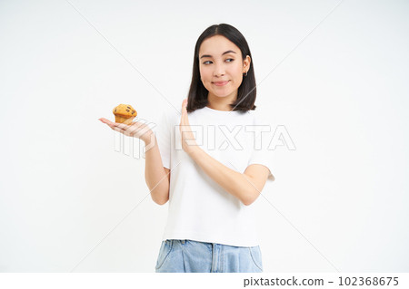 Cute asian girl with will power, refuses the cupcake, stays on diet, isolated on white background 102368675