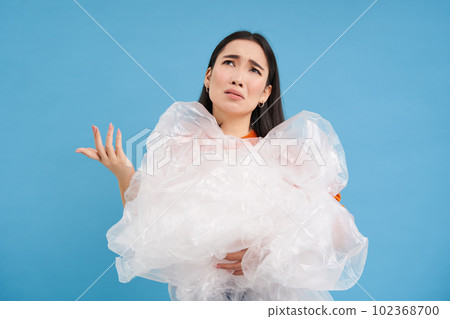 Disappointed asian woman with plastic garbage in hands, shrugging with frustrated face expression, upset with lack of recycling centers, blue background 102368700