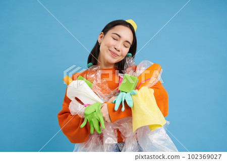 Portrait of smiling asian woman hugging empty plastic bottles and recycable garbage, eco-activist likes to recycle, blue background Portrait of smiling asian woman hugging empty plastic bottles and recycable garbage, eco-activist likes to recycle, blue background 102369027
