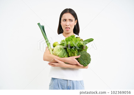 Woman with disgusted face, holding vegetables, green organic food, hates diets and detox, white background Woman with disgusted face, holding vegetables, green organic food, hates diets and detox, white background 102369056