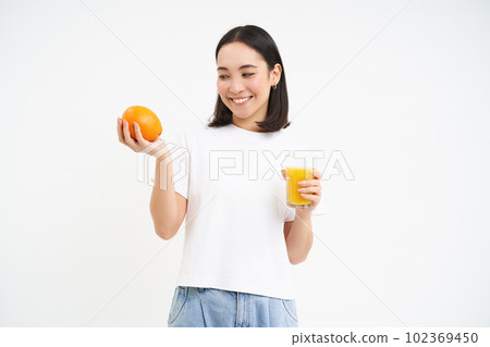 Beautiful and healthy young woman, starts her day with fresh juice, holding orange fruit and smiling, white background Beautiful and healthy young woman, starts her day with fresh juice, holding orange fruit and smiling, white background 102369450