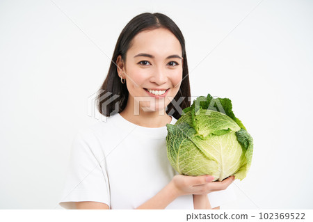 Close up portrait of young asian woman, smiling and proudly showing her self grown vegetable, holding cabbage, white background Close up portrait of young asian woman, smiling and proudly showing her self grown vegetable, holding cabbage, white background 102369522