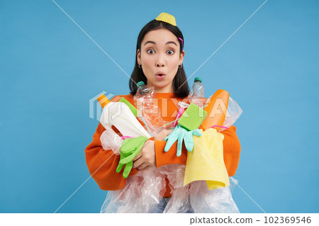 Portrait of korean woman with surprised face, holding empty plastic bottles and trash for recycling, blue background Portrait of korean woman with surprised face, holding empty plastic bottles and trash for recycling, blue background 102369546