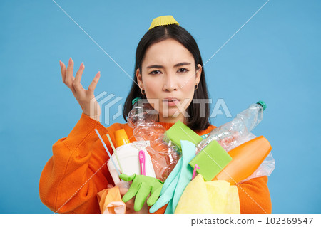 Portrait of woman puzzled by recycling rules, holding empty plastic bottles and garbage, looks complicated, blue background Portrait of woman puzzled by recycling rules, holding empty plastic bottles and garbage, looks complicated, blue background 102369547