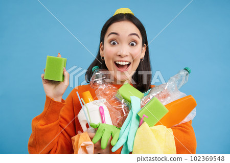 Enthusiastic asian girl showing cleaning sponge, holding empty plastic bottles, trash for recycling, sorting her household garbage, blue background Enthusiastic asian girl showing cleaning sponge, holding empty plastic bottles, trash for recycling, sorting her household garbage, blue background 102369548