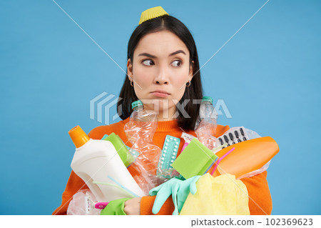 Puzzled young woman with pile of garbage, holds plastic bottles and trash for recycling, looks perplexed, blue background Puzzled young woman with pile of garbage, holds plastic bottles and trash for recycling, looks perplexed, blue background 102369623
