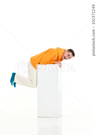 young man in orange sweatshirt sitting on white cube young man in orange sweatshirt sitting on white cube 102371249