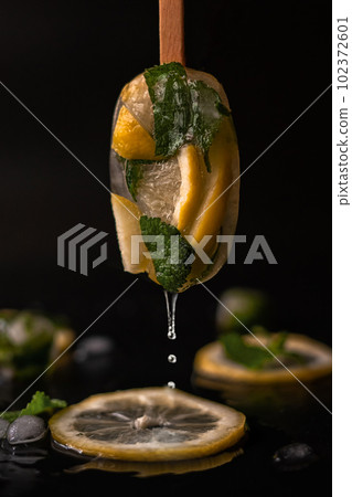 juice flowing down an Ice Pops of fruit ice with a lemon on a stick on a dark background 102372601