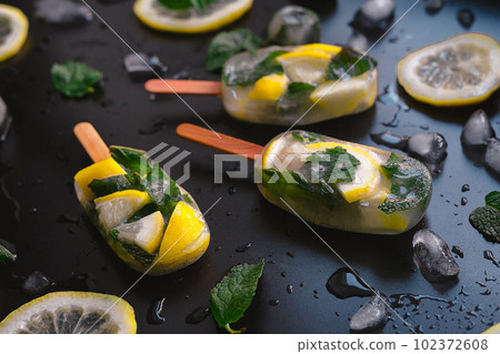 Close-up of Refreshing Fruit Ice Pops with Lemon and Mint on Dark Background 102372608